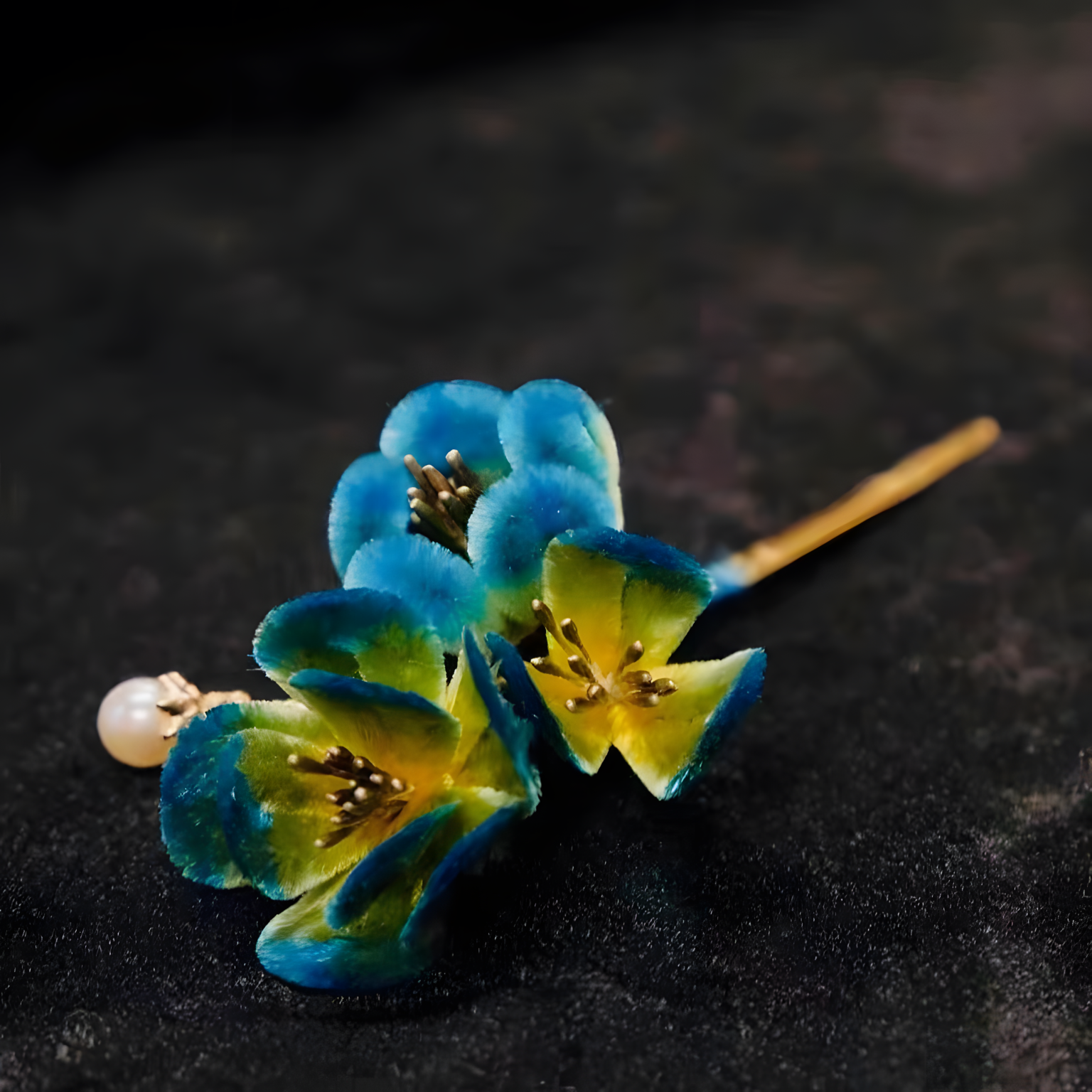 The picture shows a hairpin ornament made by the intangible cultural heritage of China - the Ronghua (velvet flower) craft. The three Ronghua flowers have unique shapes. The outer edges of the petals are blue, gradually changing to yellow - green towards the inside, presenting rich layers. The stamens are made of metal wires with dark - colored accents, giving a unique texture. A round pearl is suspended from the head of the hairpin, adding a touch of elegance. The whole piece fully demonstrates the ingenuity and delicacy of traditional craftsmanship.
