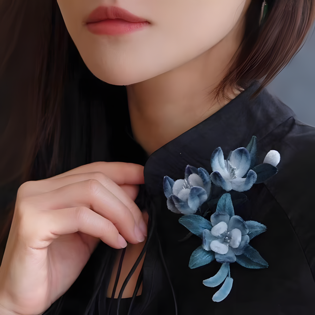 In the picture, there is a lady with brown hair, wearing a black top. She gently touches the collar with an elegant gesture. Beside the collar is an ornament made by the intangible cultural heritage of China - the Ronghua (velvet flower) craft. It consists of three velvet flowers with a blue - white gradient and several blue - green leaves. The flowers are exquisitely shaped, and the petals seem to be covered with soft fluff. The color of the leaves complements that of the flowers, looking harmonious and natural. The whole ornament adds a splash of color to the black top, not only showing the exquisiteness of traditional craftsmanship but also a sense of fashion, blending perfectly with daily wear.