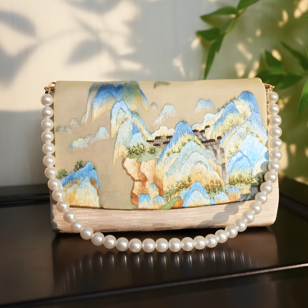 This is an embroidered landscape pearl chain bag. The bag body presents a landscape picture with delicate embroidery, rich in color layers, integrating the artistic conception of Chinese landscapes into the bag. Matched with a round pearl chain, the classic embroidery collides with the gentle pearls, combining Oriental charm and fashion sense, suitable for various styles such as Hanfu and national - style outfits.